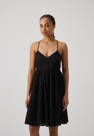 Svart kjole med tynne stropper og V-hals. Har blomsterutskjæringer, tettsittende bodice og A-linje skjørt, laget av lett stoff.