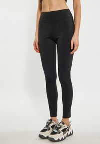 Leggings neri con vita alta, design aderente, texture liscia e dettagli cuciti. Abbinati a sneaker chunky grigio e nero.