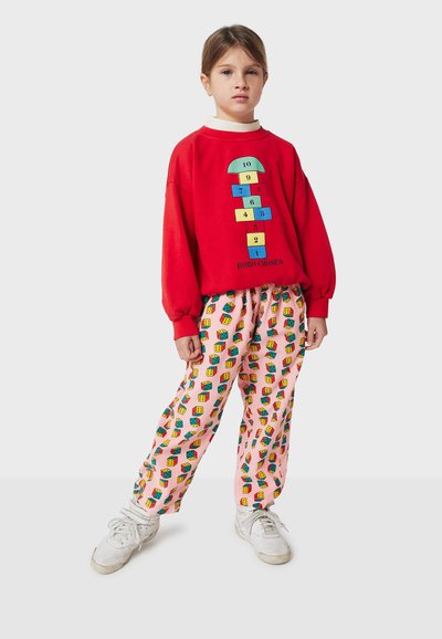 Sweatshirt rouge avec graphique de marelle ; pantalon rose avec motifs colorés en blocs ; baskets blanches ; coupe décontractée et oversize.