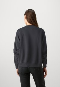 Sweatshirt gris foncé avec une coupe décontractée, des poignets et un ourlet côtelés. Présente un logo subtil à l'arrière, fabriqué à partir d'un matériau doux.