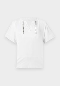 Άσπρο τοπ με κοντά μανίκια και V-λαιμόκοψη, με μαύρα και λευκά στριφτά κορδόνια που κρέμονται από μεταλλικά κουμπώματα στο λαιμό.