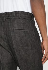 Svarta jeans med resårmidja, med en bakficka och ett slätt, strukturerat tyg. Den övergripande designen är avslappnad och funktionell.