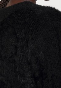 Närbild av en person som bär en texturerad svart fluffig tröja, som framhäver tygets mjuka och fluffiga yta.