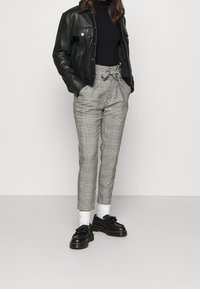 Black leather jacket, fitted black turtleneck, gray checkered trousers with bow tie at the waist, black shoes, and white socks.