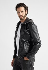 Svart läderjacka med en grå hoodie. Har dragkedja fram, sidofickor och en smal passform. Texturen är slät med en subtil glans.