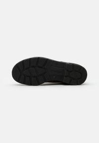 Suela de goma negra de un zapato con un patrón texturizado, con surcos profundos y una forma redondeada para tracción y estabilidad.