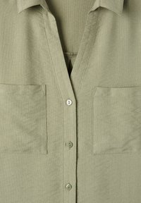 Camicia verde oliva con colletto a V, due tasche frontali e chiusura con bottoni. Tessuto morbido e testurizzato, con dettagli di cucitura sottili.