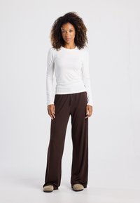 White long-sleeve shirt with round neck, paired with brown wide-leg pants. Soft fabric; pants have a drawstring waist and loose fit.