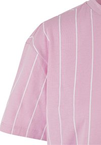 Svetle růžové tričko s vertikálními bílými pruhy, vyrobené z měkké bavlny, s kulatým výstřihem a krátkými rukávy.