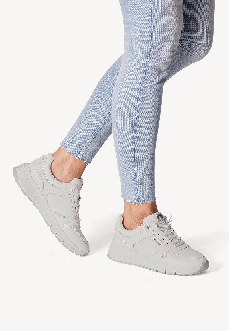 Baskets grises claires avec une texture lisse, un design à lacets et un col rembourré. Posées sur un jean bleu clair avec un ourlet effiloché.