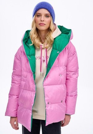 Różowa puchowa kurtka z zielonym wykończeniem i kapturem, z zapięciami na zatrzaski i pikowaną strukturą, noszona na beżowym hoodie z troczkami.