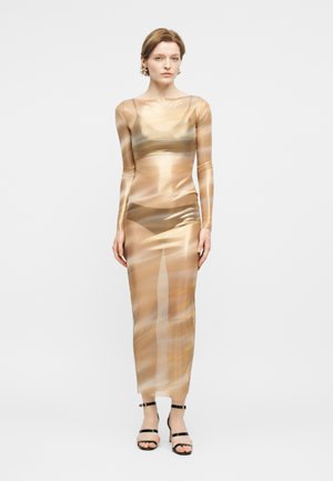 Naine kannab pikka, läbipaistvat, kehale istuvat kleiti, millel on abstraktsed beeži ja pruuni mustriga mustad rihmlised kontsakingad ning lühikesed juuksed.