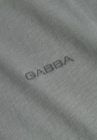 Szürke szövet finom textúrával, a megfelelő árnyalatban megjelenő, relief mintás "GABBA" logóval, hangsúlyozva a minimalista dizájnt.