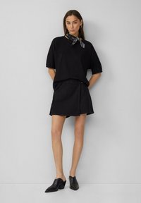 Czarny t-shirt z krótkim rękawem i bufiastymi rękawami, zestawiony z czarną spódnicą dżinsową. Obuwie to czarne, wyższe klapki. Szalik związany wokół szyi.