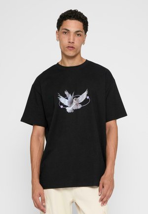 Black cotton T-shirt featuring a front graphic of a white dove with extended wings, surrounded by a circular line and colored dots.