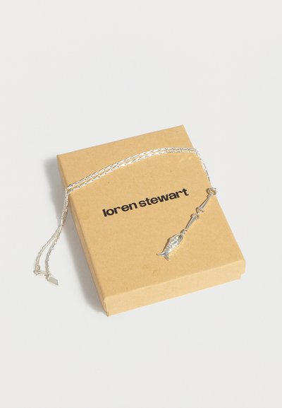 Ασημένιο κολιέ με αλυσίδα και μενταγιόν σε σχήμα ψαριού, ακουμπισμένο σε καφέ κουτί με την ετικέτα «loren stewart» σε λευκό φόντο.