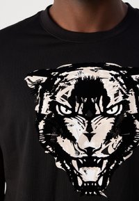 Černé bavlněné tričko s velkým tigerem v bílé a černé barvě, které zobrazuje ostré detaily a výrazné linie přes hruď.