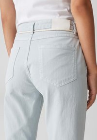 Jean bleu clair avec une coupe décontractée, dotés de deux poches arrières, de coutures discrètes et d'une boucle de ceinture en tissu. Texture lisse et matériau durable.