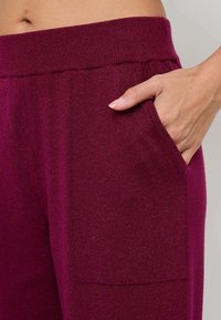 Jogging en tricot bordeaux avec une texture douce, une taille élastique et une poche sur le côté. Le tissu a un léger éclat.