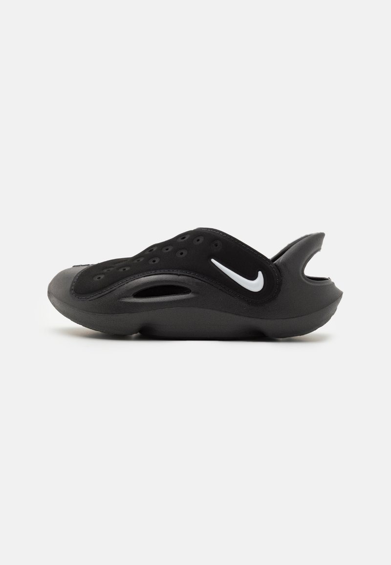 Black footwear with a sleek design, featuring a smooth texture, perforated upper, and a distinct white logo on the side.
