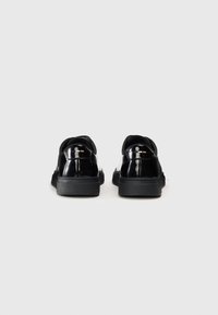 Chaussures en cuir verni noir avec un bout arrondi, semelle en caoutchouc et design à enfiler, présentant des accents noirs au talon et sur la languette.