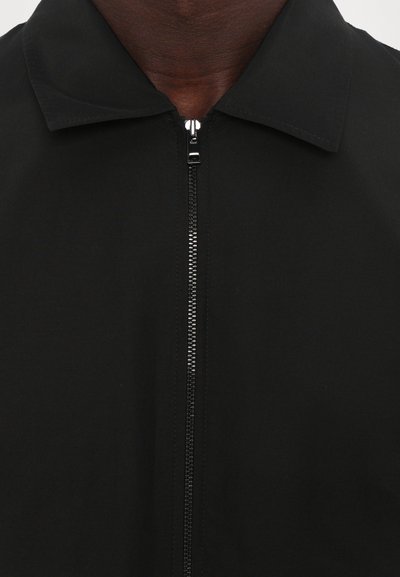 Zwarte zip-up jack met een opgevouwen kraag, met een gladde textuur en een metalen rits in het midden.