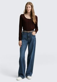 Bordeaux langärig shirt met ribbeltextuur, knoopdetail bij de halslijn; gecombineerd met hoog-waist, wijde blue jeans en witte sneakers.
