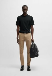 Black polo shirt, beige slim-fit trousers, sleek black shoes, and a dark gray bag. Smooth texture, clean lines, and minimal design.