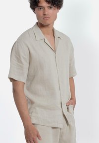 Korte mouwen beige linnen shirt met een ontspannen pasvorm, enkele zak en een gladde textuur, met een klassieke kraag en knoopsluiting.