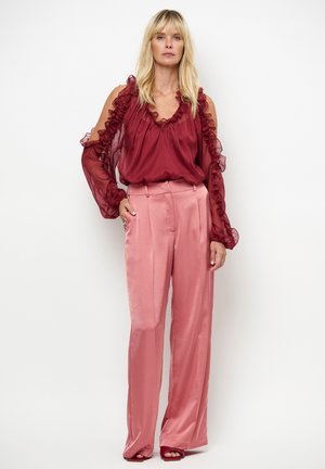 Blouse transparente bordeaux avec manches à volants associée à un pantalon taille haute en satin rose pâle. Texture lisse, drapé élégant et silhouette ajustée.