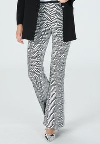 Black and white zigzag patterned flared pants made of a lightweight fabric, paired with a black blazer and silver pointed shoes.