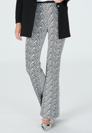 Black and white zigzag patterned flared pants made of a lightweight fabric, paired with a black blazer and silver pointed shoes.