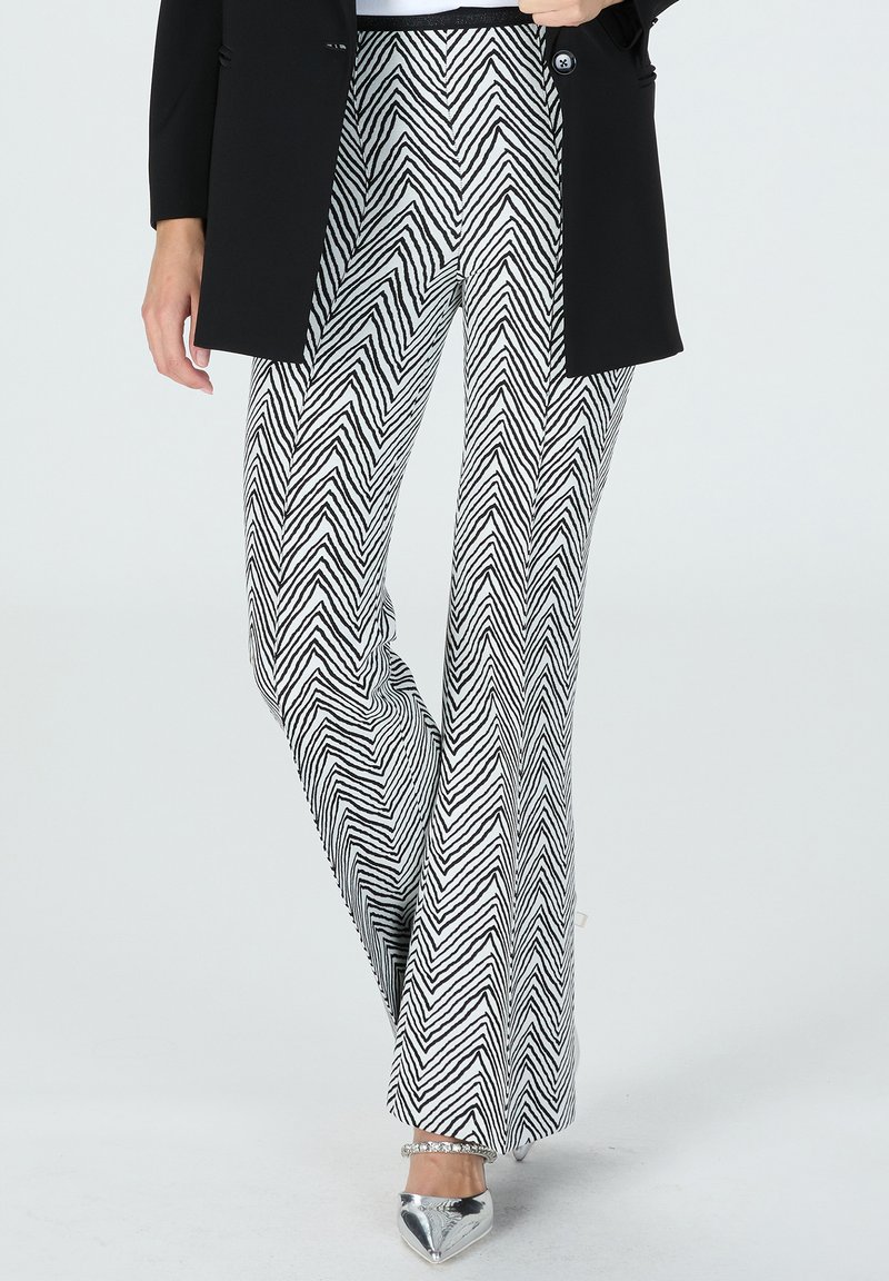 Black and white zigzag patterned flared pants made of a lightweight fabric, paired with a black blazer and silver pointed shoes.