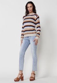 Knit sweater with multicolored horizontal stripes in brown, blue, and white. Paired with light blue jeans and brown platform sandals.