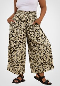 Beige leveletasot, joissa on musta leopardi-printti, elastisella vyötärönauha ja sivutaskut. Yksi lahkeista on hieman rutistettu helmasta.