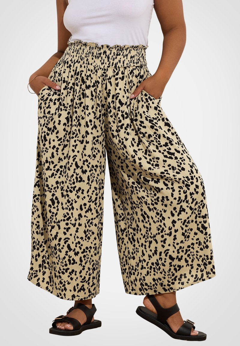 Beige leveletasot, joissa on musta leopardi-printti, elastisella vyötärönauha ja sivutaskut. Yksi lahkeista on hieman rutistettu helmasta.