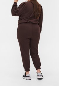 Brauner, passend gestalteter Kapuzenpulli und Jogginghose aus weichem Stoff. Der Kapuzenpulli hat puffige Ärmel; die Jogginghose hat elastische Bündchen und Seitentaschen.