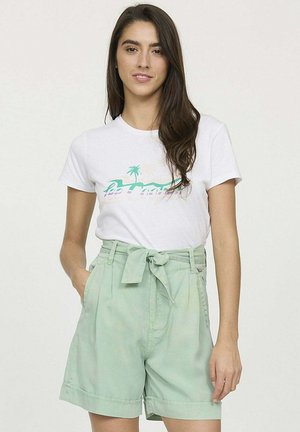 Un t-shirt blanc avec un motif graphique vert associé à un short taille haute vert menthe avec une ceinture en tissu et des poignets retroussés.