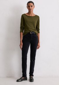 Długo-sleeve oliwkowa bluzka w połączeniu z czarnymi spodniami z korduroju, charakteryzującą się dopasowanym krojem oraz czarnymi skórzanymi loafersami, podkreśloną czarnym paskiem.