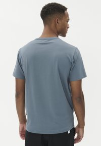 Šedé tričko s krátkým rukávem vyrobené z měkké a lehké látky. Má kulatý výstřih a rovný lem, s malou etiketou na dolní levé straně.