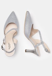Chaussures à talons aigus argentées pailletées avec un bout pointu, un design à lanières, une boucle à la cheville ajustable et un talon gris métallique.