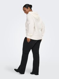 Ljusbeige luvtröja med oversized passform och ribbade mudd, kombinerad med svarta utsvängda jeans och svarta ankelboots.