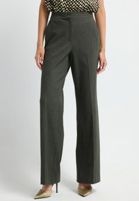 Femme portant un pantalon droit taille haute gris foncé avec un haut à carreaux et des escarpins beiges à bouts pointus, se tenant sur un fond clair.