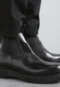 Botas Chelsea negras de cuero con paneles laterales elásticos, suela de goma texturizada y acabado suave. Diseño sencillo, primer plano en los pies.