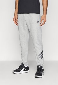 Grå sweatpants med resårmidja, med en tre-stripes accent i svart på sidan och en Adidas-logotyp i grått.