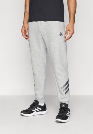 Pantaloni de trening gri cu o talie elastică, având un accent cu trei dungi negre pe lateral și un logo Adidas gri.