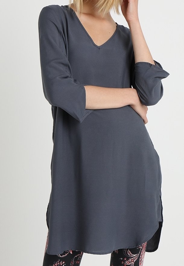 Szara tunika z 3/4 rękawem i dekoltem w serek, wykonana z miękkiego materiału. Charakteryzuje się luźnym krojem i bocznymi rozcięciami, zestawiona z wzorzystymi legginsami.