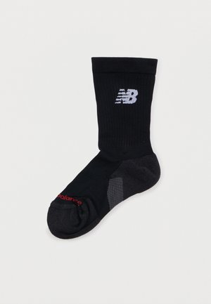 Calcetín negro tipo tripulación con el logotipo "NB" blanco en el puño y texto rojo "balance" cerca de la punta, con áreas acolchadas y reforzadas.