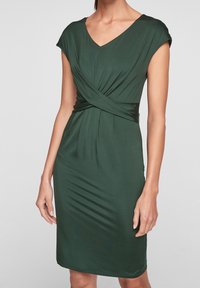 Mörkgrön figurnära klänning med V-ringning, korta ärmar och vridningsdetalj vid midjan; slät textur och knälång design.