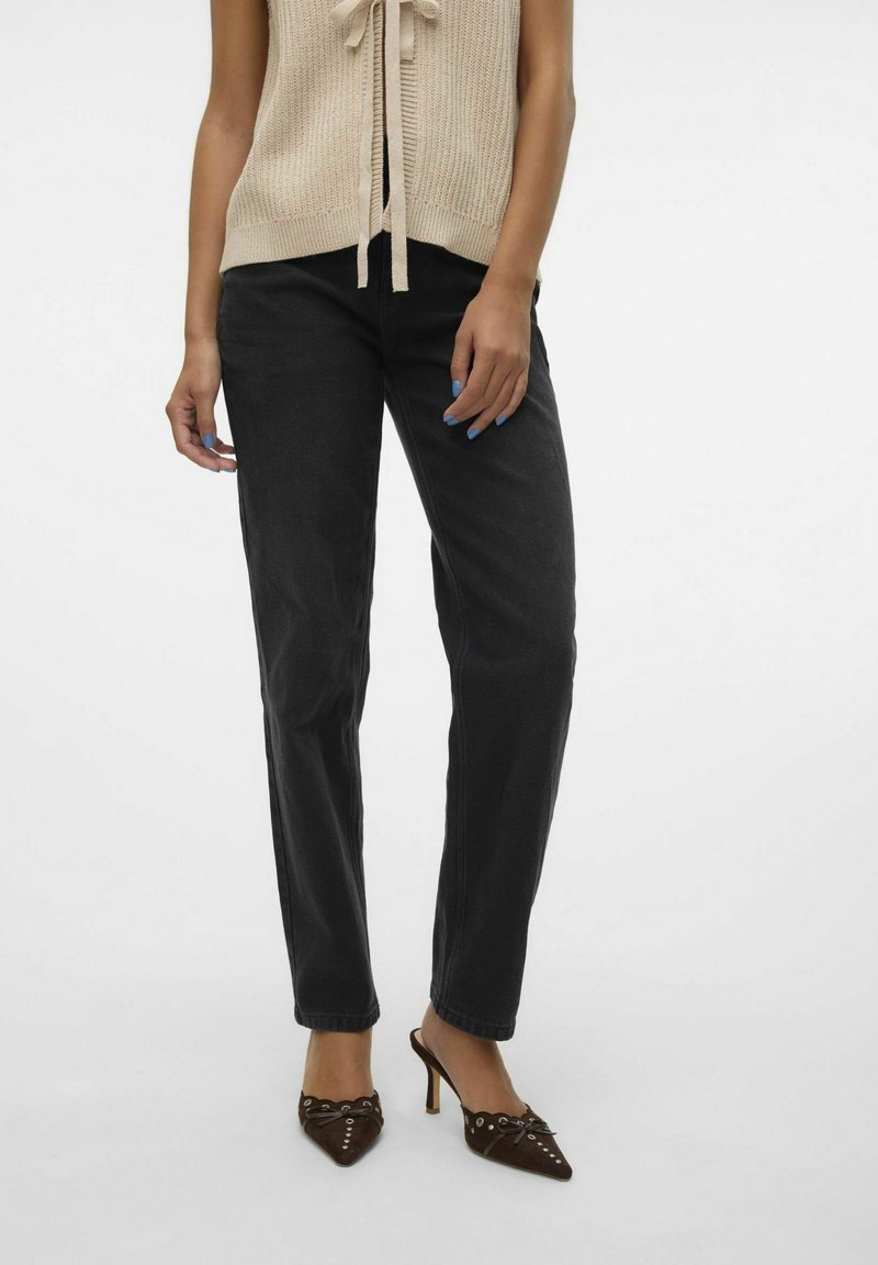 Sort denim jeans med lige pasform, parret med en beigefarvet strikket top med en sløjfedetalje. Brune hæle mules med detaljer.